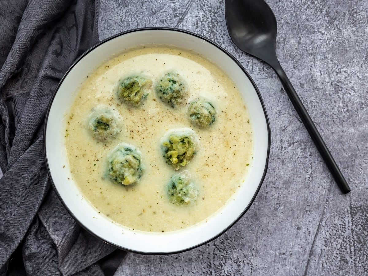 Eine runde Schüssel gefüllt mit Kohlrabi-Cremesuppe neben einem grauen Geschirrtuch.