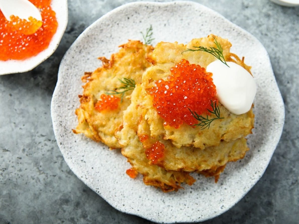 Ein weißer Teller mit Latkes auf einem grauen Tisch.