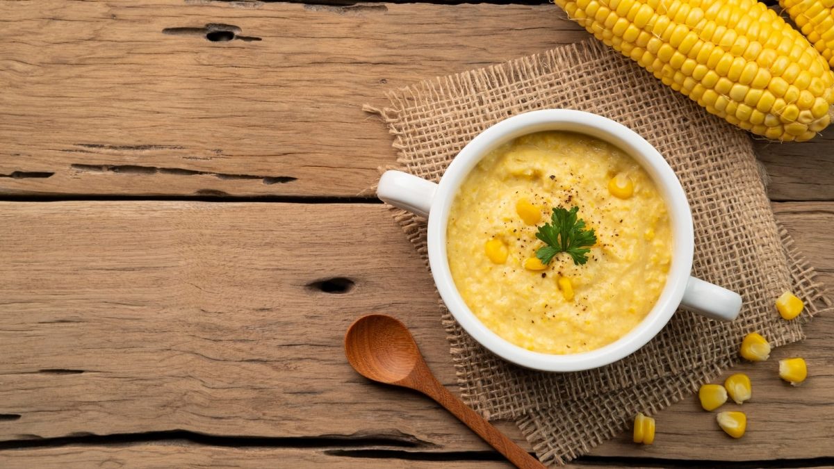 Eine weiße Schüssel mit Corn Potage auf einem Holztisch.