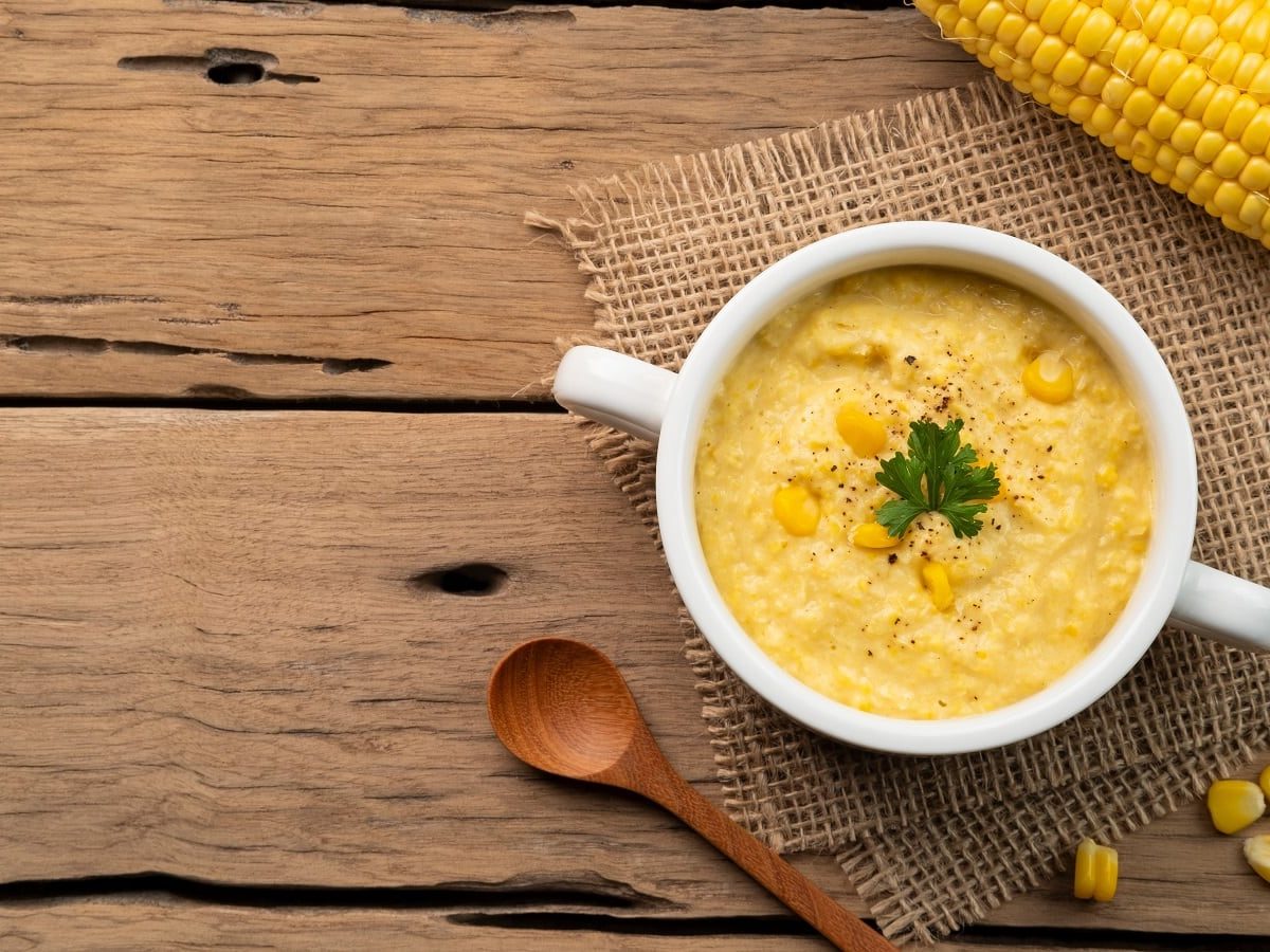 Eine weiße Schüssel mit Corn Potage auf einem Holztisch.