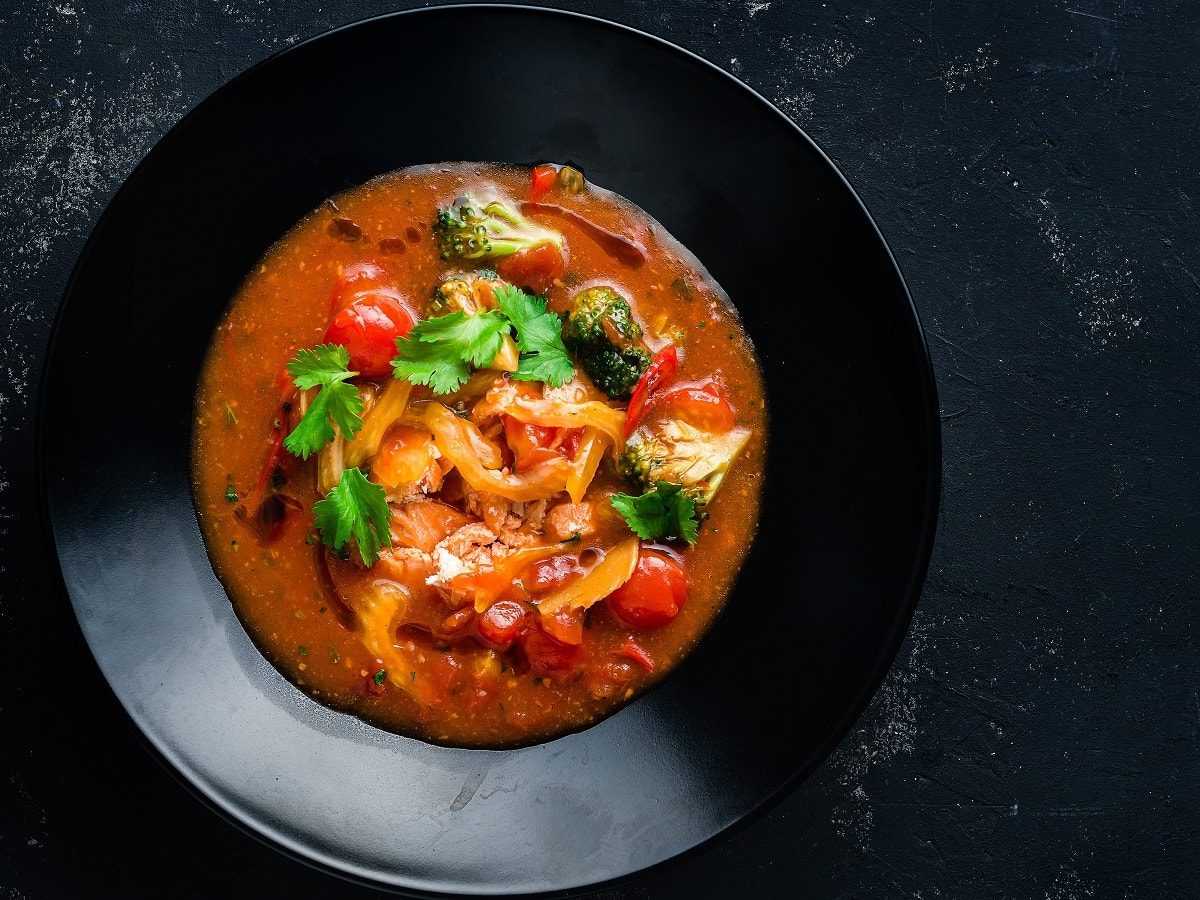 Eine schwarze Schüssel auf einem dunklen Tisch mit vietnamesischer Gemüsesuppe mit Lachs.