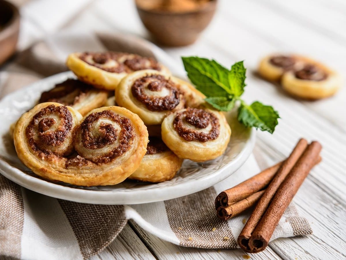 Ein Teller mit Zimt-Palmiers auf einem weißen Holztisch.