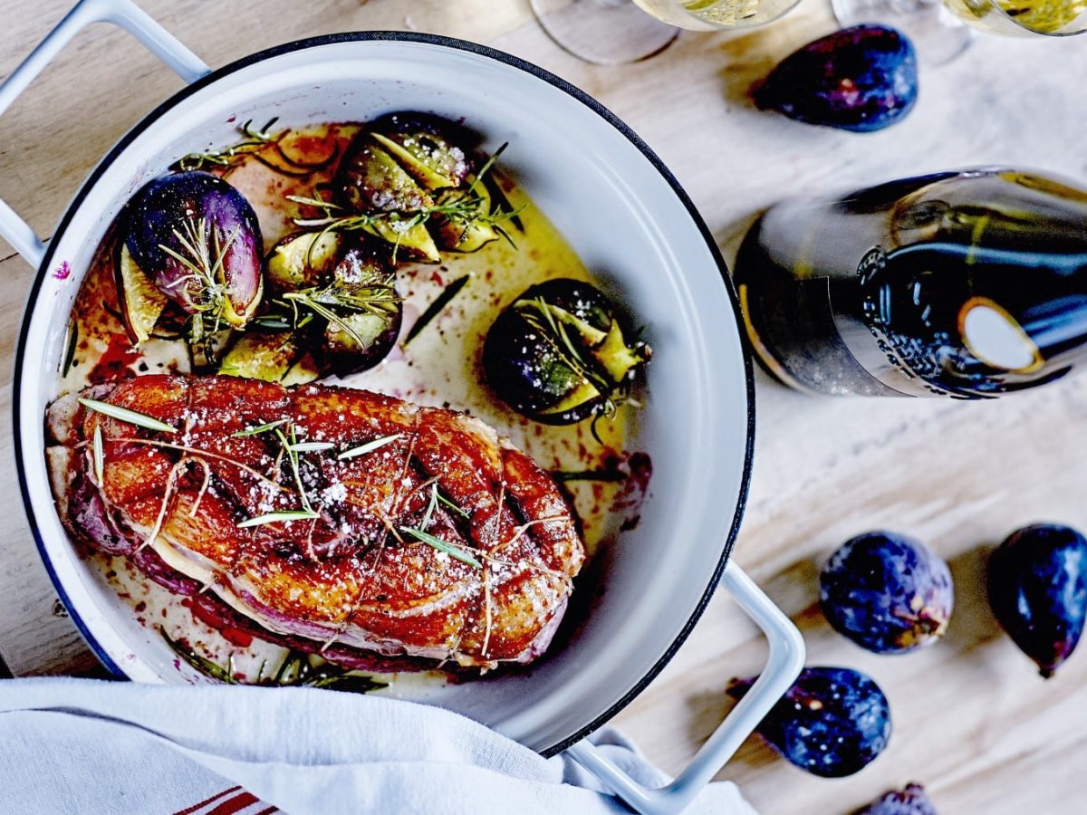 Entenbrust-Cordon-Bleu mit Rosmarin-Feigen im Topf neben Feigen und Weinflasche auf Holz.