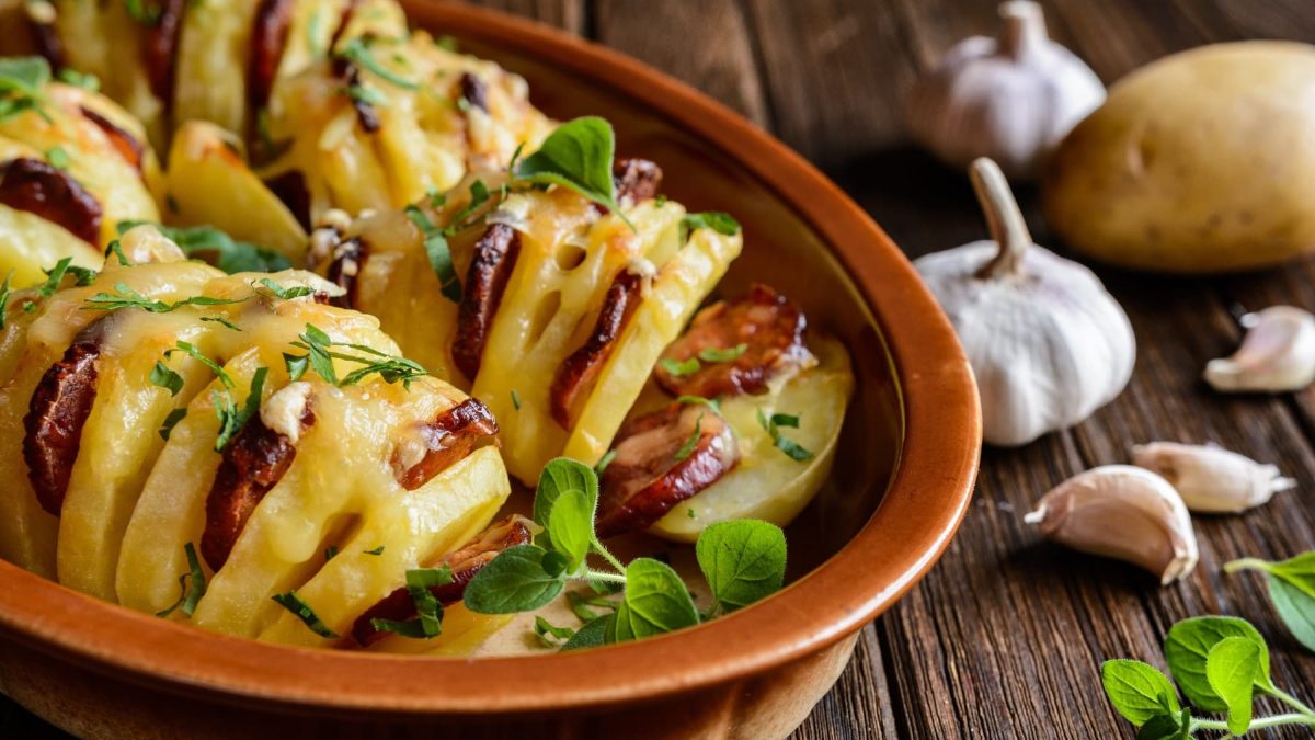 Mehrere Kartoffeln mit Einritzungen in einer Ofenform. In den Schlitzen ist die Chorizowurst und alles wurde mit Käse überbacken.