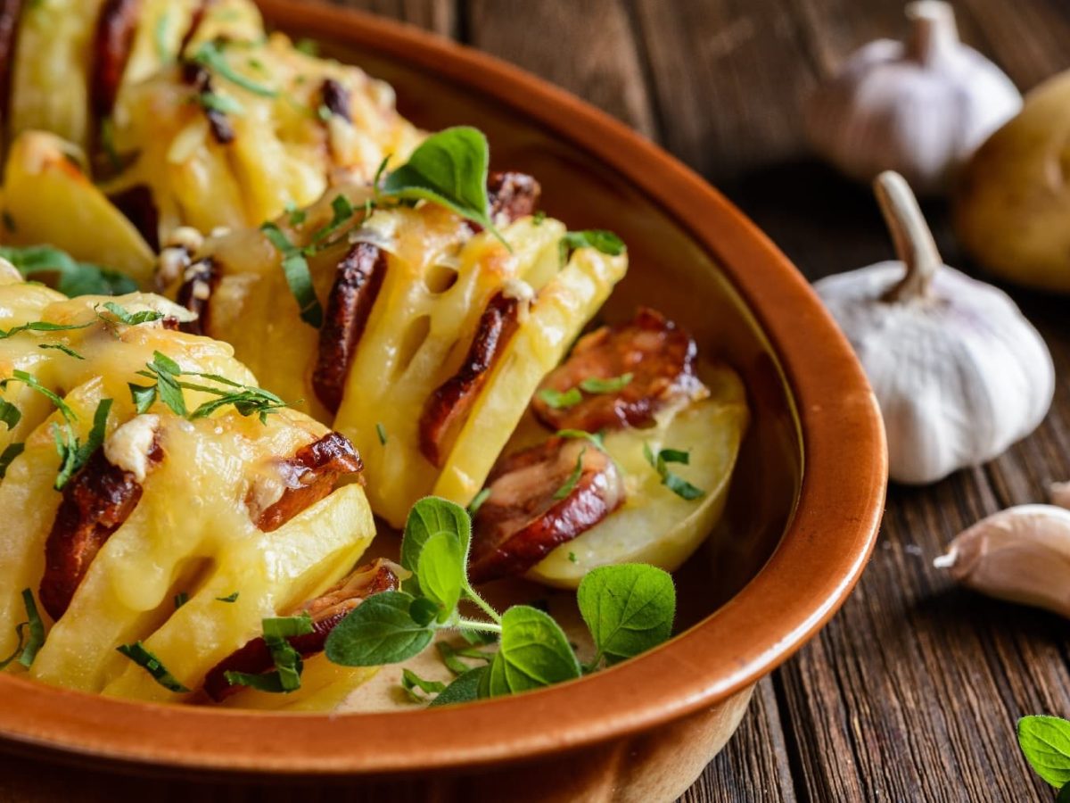 Mehrere Kartoffeln mit Einritzungen in einer Ofenform. In den Schlitzen ist die Chorizowurst und alles wurde mit Käse überbacken.