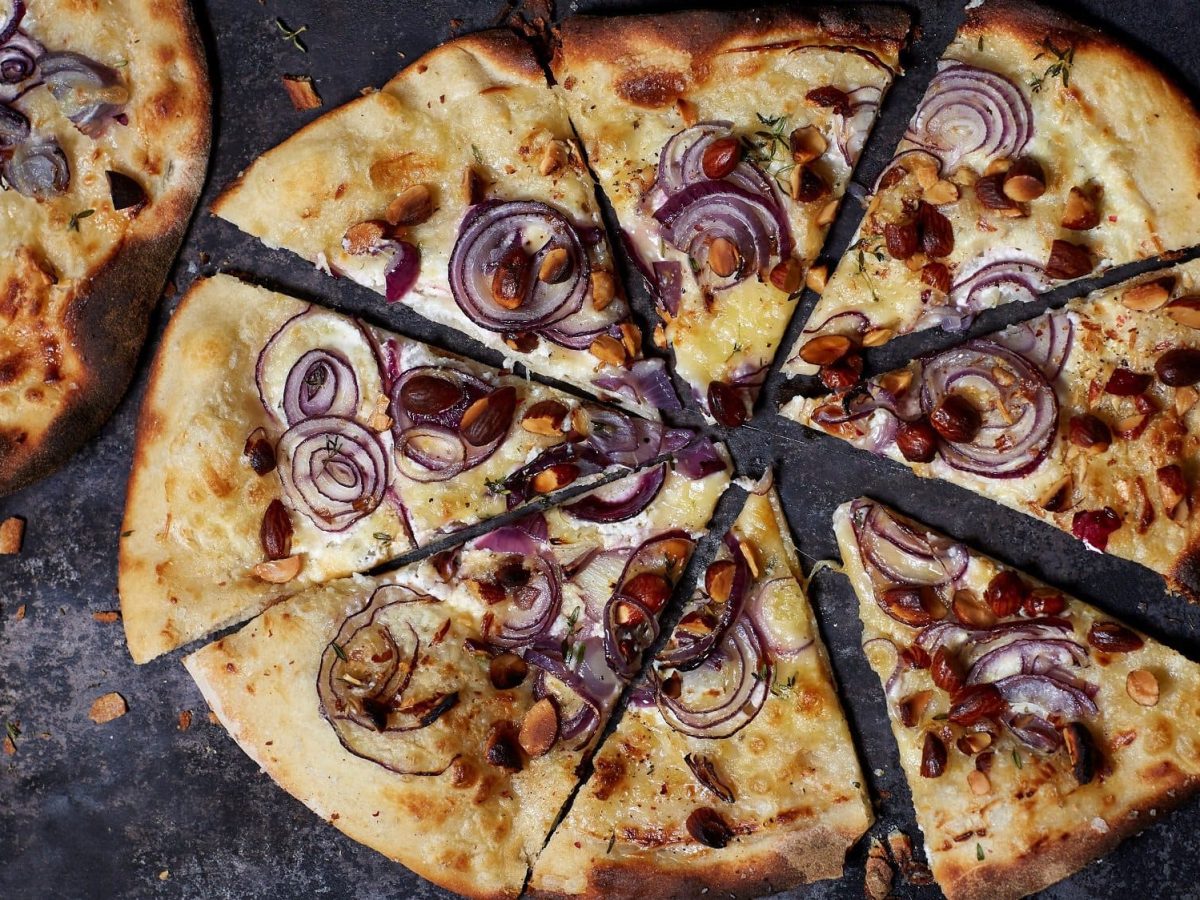 Ein geschnittener Flammkuchen mit Räuchermandeln und roten Zwiebeln.