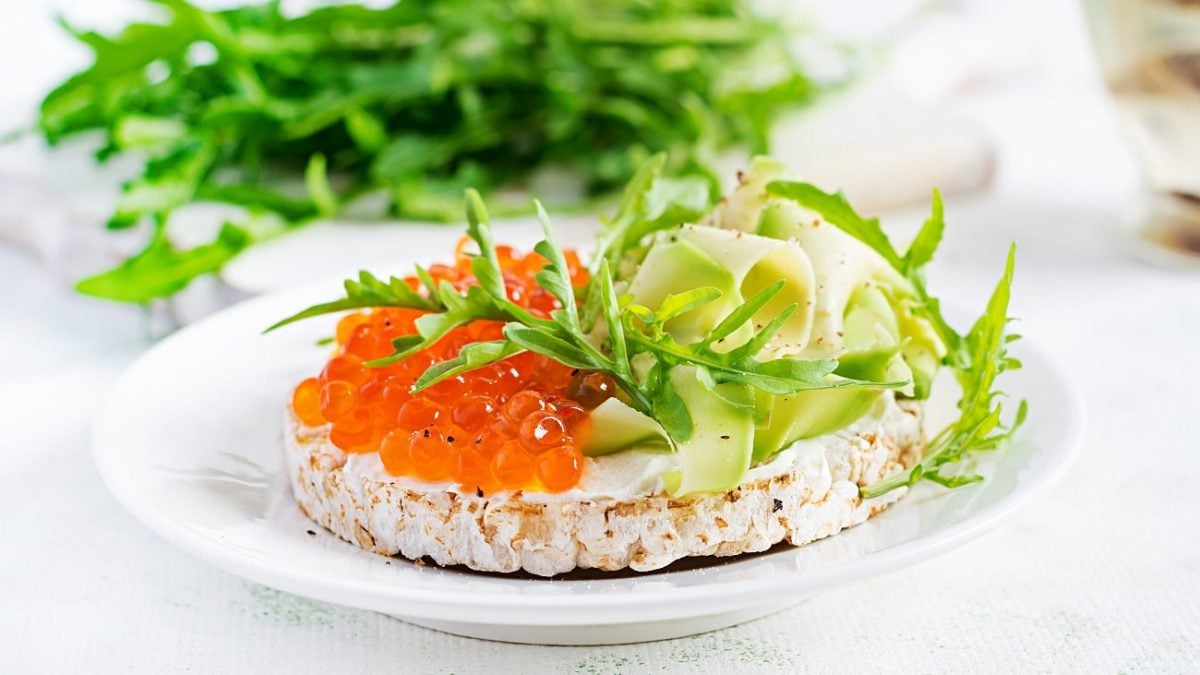 Frontalsicht: eine Frühstückswaffel mit Forellenkaviar und Rucola liegt auf einem hellen teller.