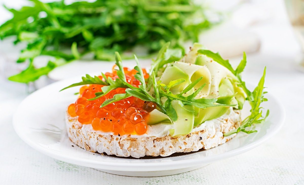 Frontalsicht: eine Frühstückswaffel mit Forellenkaviar und Rucola liegt auf einem hellen teller.