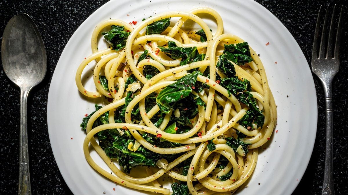 Ein Teller Grünkohl-Pasta mit Zitrone in der Draufsicht, links und rechts daneben Löffel und Gabel.