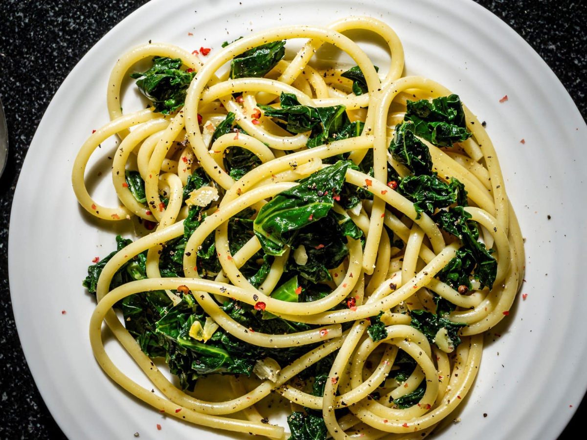 Ein Teller Grünkohl-Pasta mit Zitrone in der Draufsicht, links und rechts daneben Löffel und Gabel.