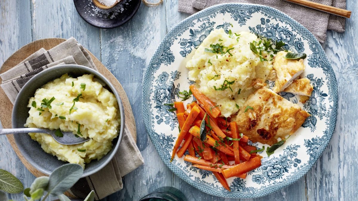 Hähnchenschnitzel in Eihülle mit Selleriepüree und Möhren in der Draufsicht.