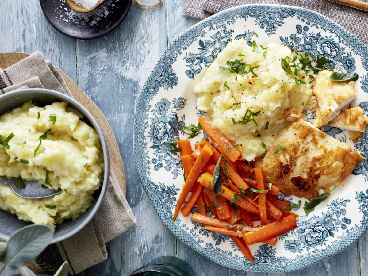 Hähnchenschnitzel in Eihülle mit Selleriepüree und Möhren in der Draufsicht.