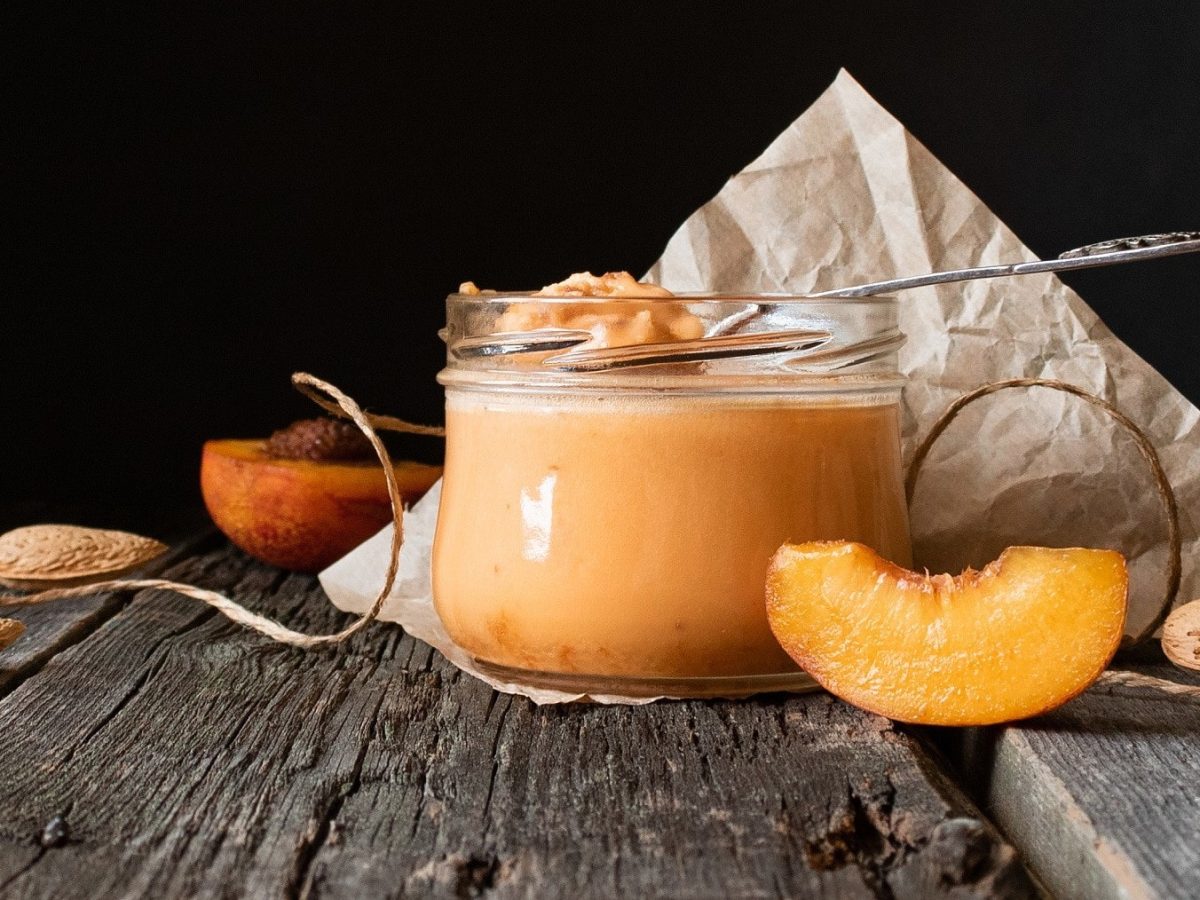 Honig-Creme mit Aprikosen und Mandelmus, serviert in einem kleinen Dessertglas auf einem rustikalen Holztisch.