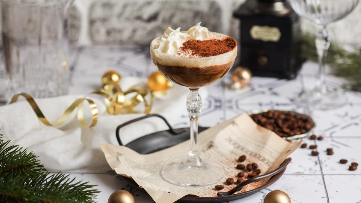 Ein hohes Glas mit dem Hot White Russian auf einem weißen Tisch mit Kaffeebohnen.