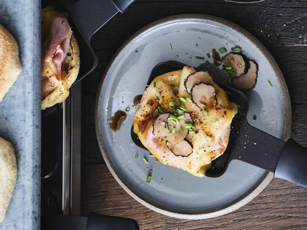 Karlsbader Schnitte, mit Käse überbackenes Schinkentoast mit Trüffel und Worcestersauce auf einem Raclette-Pfännchen serviert.