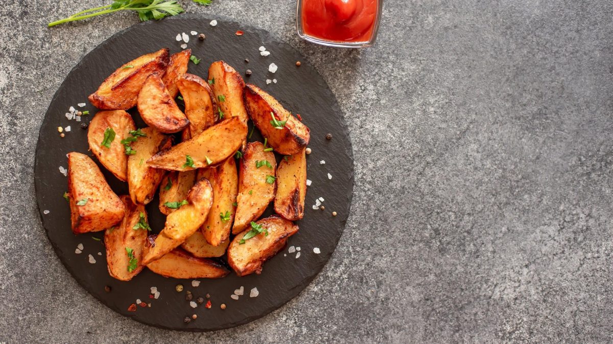 Kräuter-Knoblauch-Kartoffelecken auf einem Schieferteller, bestreut mit Petersilie und grobem Salz, in der Draufsicht.