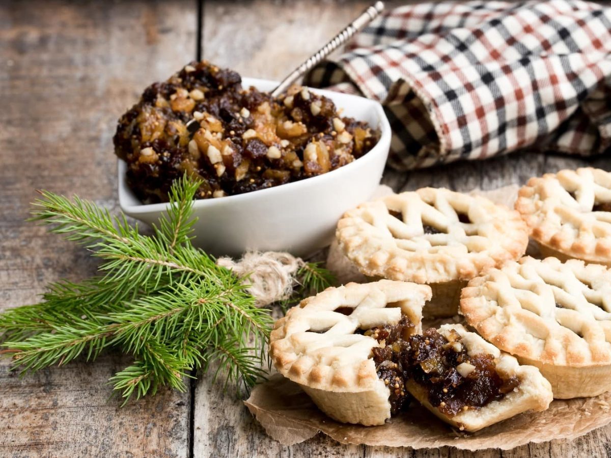 Mincemeat Pies mit frichem Mincemeat, bestäubt mit Puderzucker und angebrochen serviert auf einem hölzernen Tisch mit weihnachtlichem Dekor.