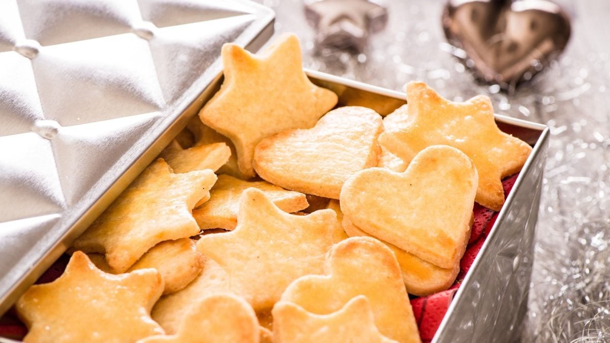 Eine geöffnete Keksdose mit Orangenplätzchen in Herz- und Sternform.