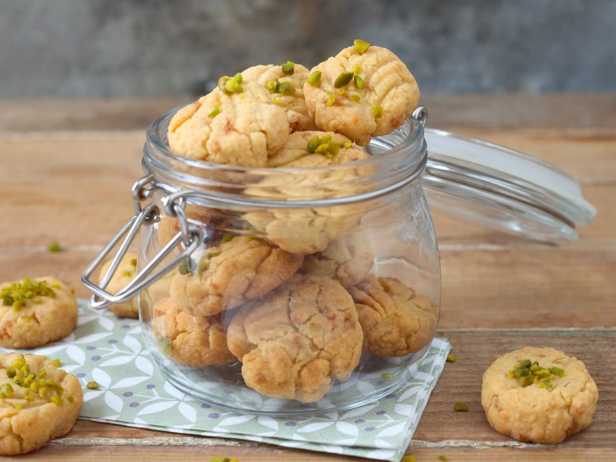 Ein offenes Glas Pistazien-Plätzchen auf einer Serviette, daneben liegen ein paar Plätzchen.