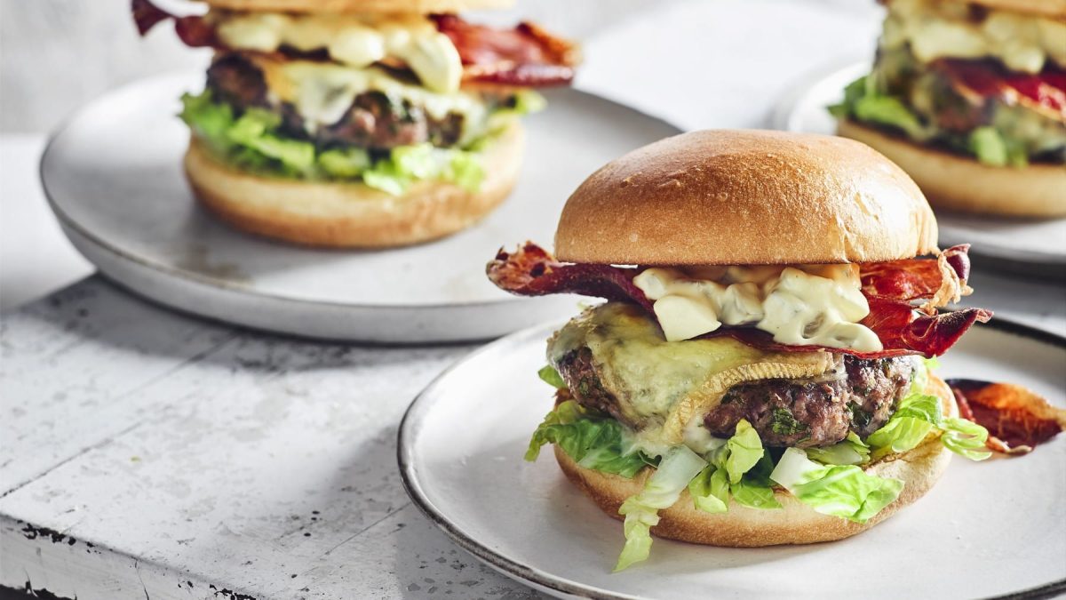 Mehrere Raclette-Burger auf weißen Tellern vor hellem Hintergrund.