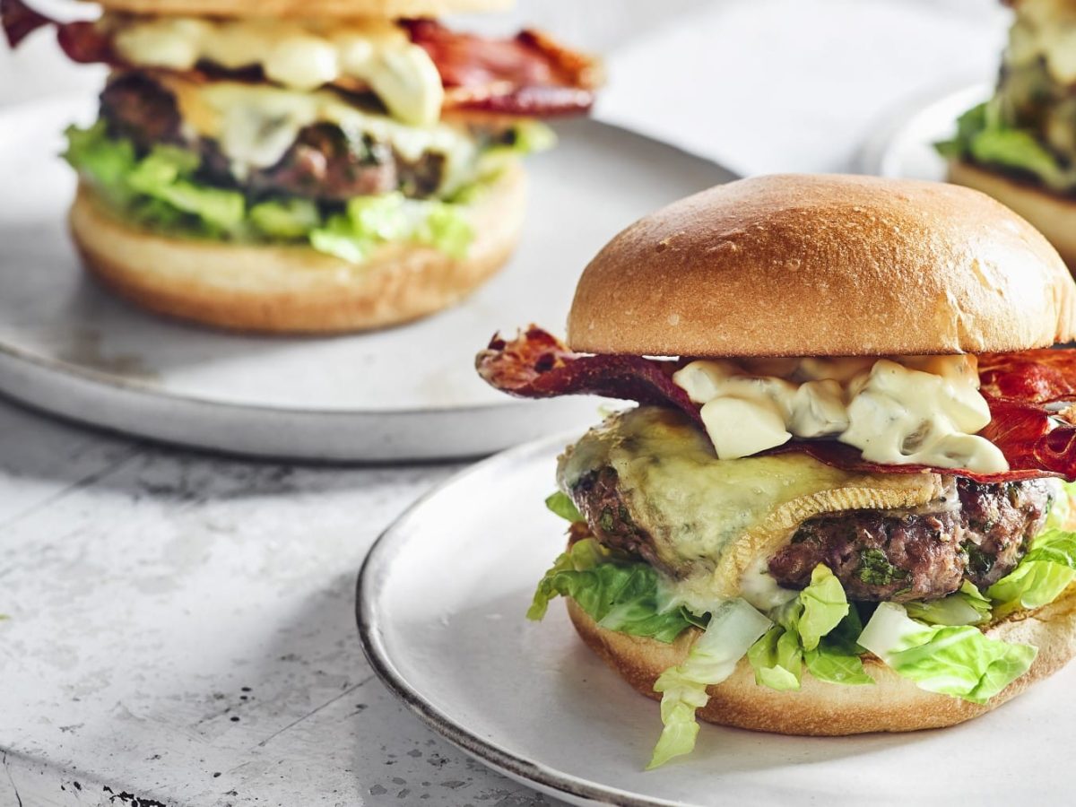 Mehrere Raclette-Burger auf weißen Tellern vor hellem Hintergrund.