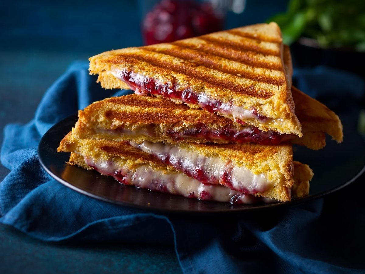 Halbierte Toastscheiben mit dem Käse und Cranberry-Senf auf dunkelblauem Untergrund.