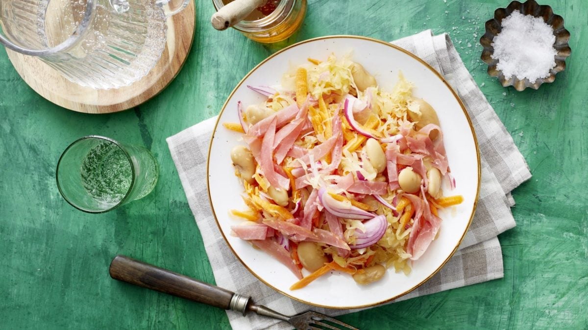 Sauerkraut-Salat mit weißen Bohnen auf einem weißen Teller mit grünem Hintergrund in der Draufsicht.