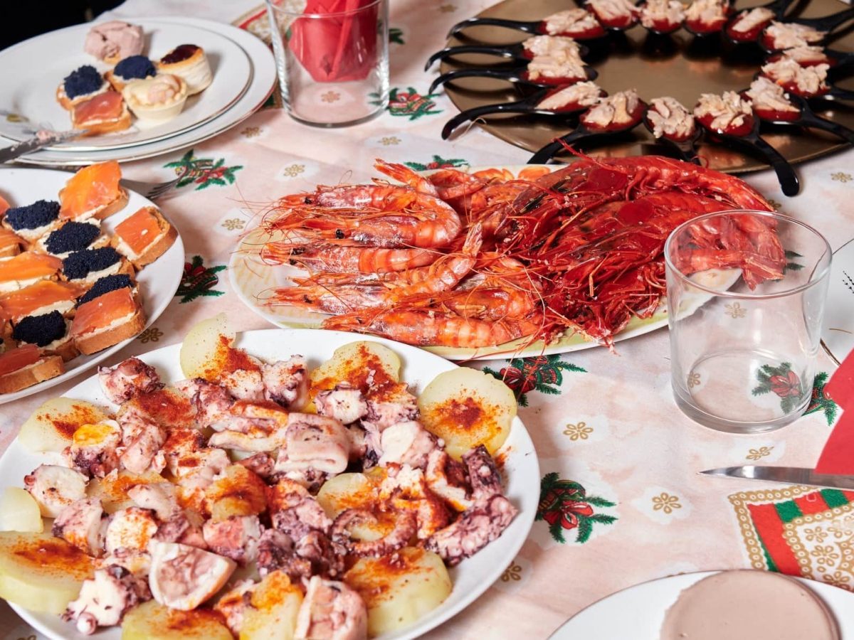 Spanisches Weihnachtsessen aus diversen Speisen auf Tellern und Häppchen auf gedecktem Tisch. Draufsicht.