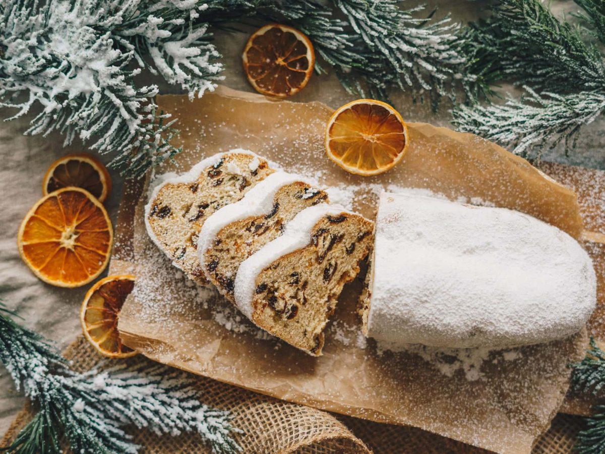 Ein angeschnittener Christstollen auf einem Schneidebrett. Drum herum weihnachtliche Dekoration.