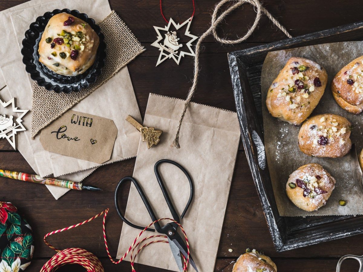 Stollenkonfekt mit Marzipan und selbst eingelegten Rumrosinen auf Backblech. Im Bild Geschenkutensilien und Weihnachtsschmuck. Draufsicht.