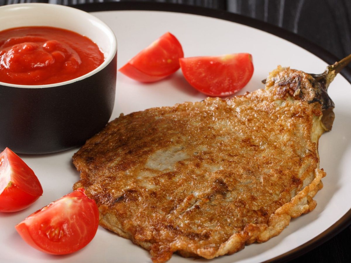 Tortang Talong philippinisches Auberginen-Omelett mit Tomaten und einer Schale Ketchup auf weißem Teller. Draufsicht.