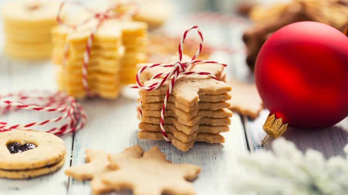 Ein Stapel vegane Plätzchen zum Ausstechen, zusammengebunden mit rot-weißem Band. Daneben eine rote Christbaumkugel.