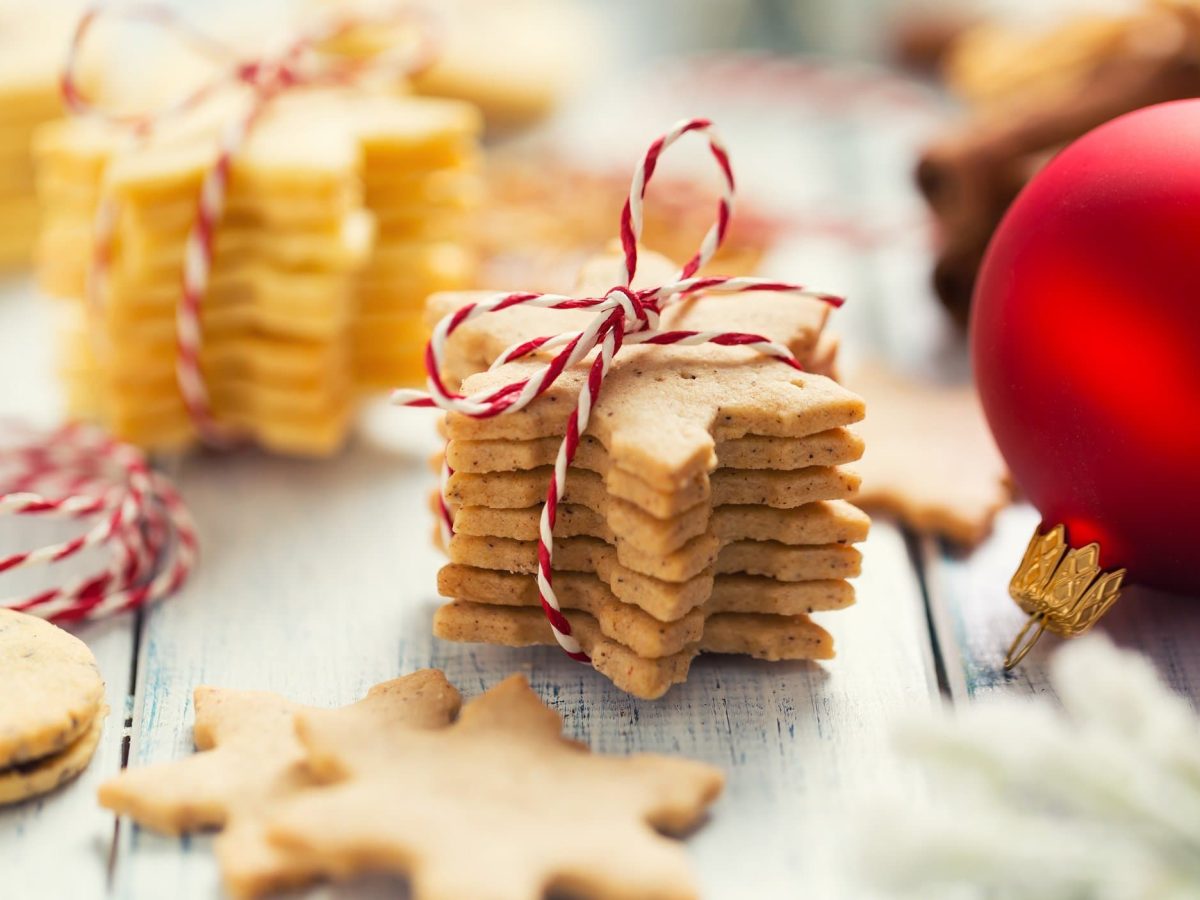 Ein Stapel vegane Plätzchen zum Ausstechen, zusammengebunden mit rot-weißem Band. Daneben eine rote Christbaumkugel.