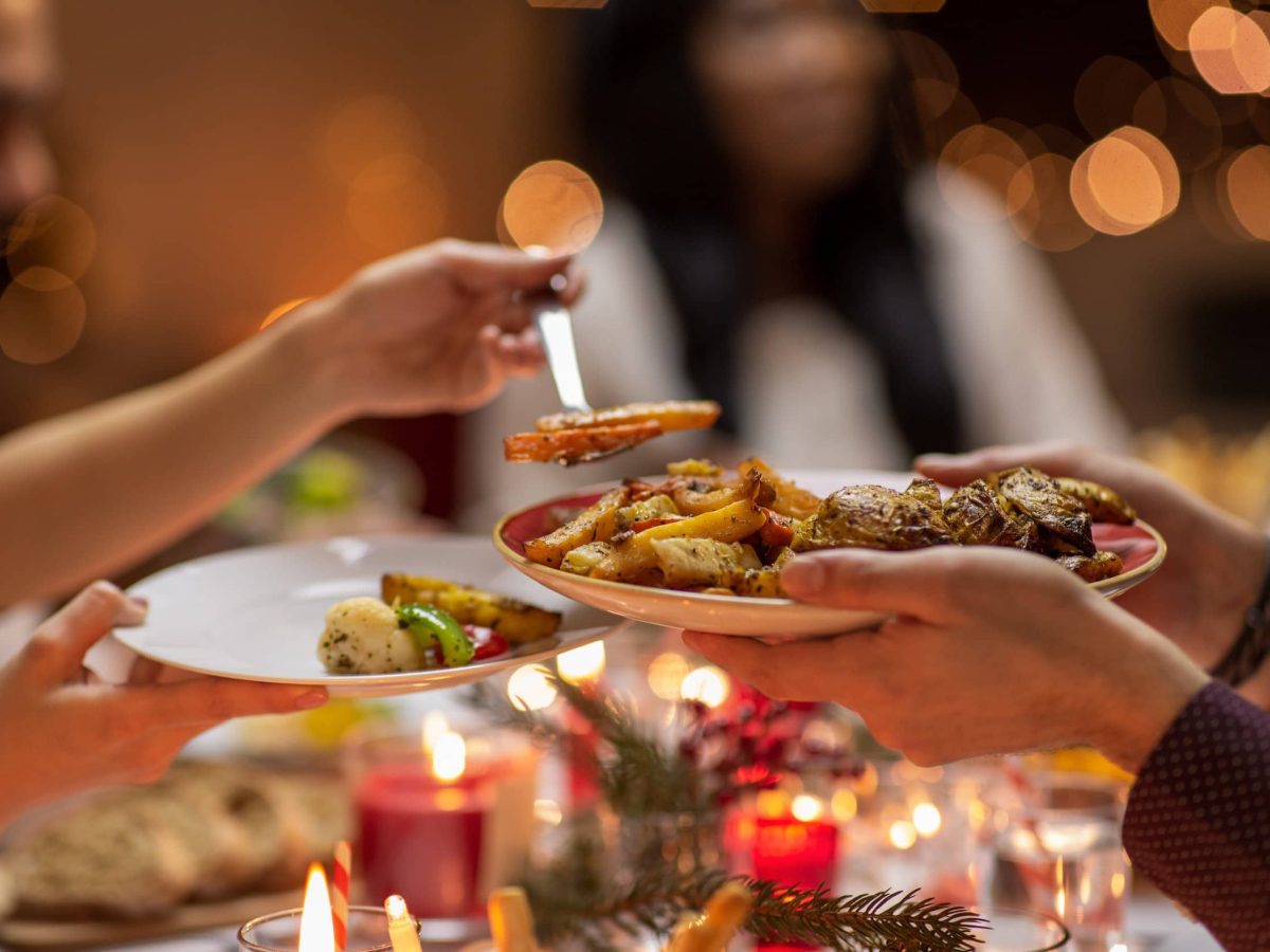 veganes Weihnachtsdinner: eine Frau füllt einem Gast Essen auf einen Teller.