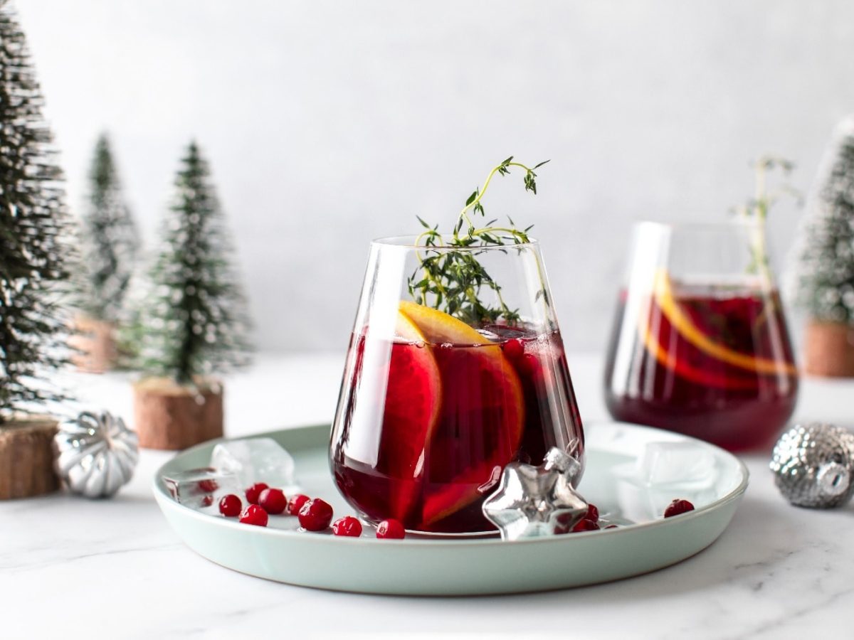 Zwei Gläser vom weihnachtlichen Gin Tonic vor einem weihnachtlichen Hintergrund mit Tannen, silbernen Kugeln und Schnee.