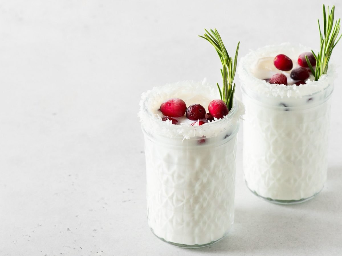 Zwei Gläser White Christmas Margarita mit Kokosraspeln, Rosmarin und Cranberrys garniert.