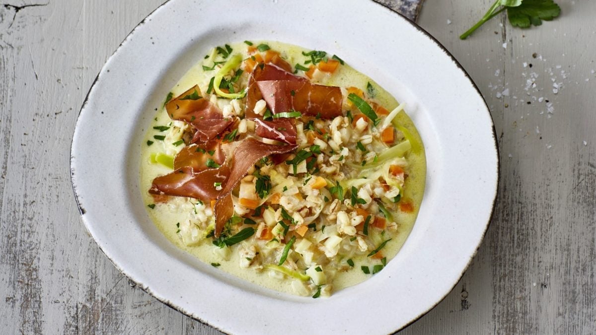 Gerstentopf mit Bündner Fleisch garniert, serviert in einer weißen tiefen Schale und bestreut mit frischer Petersilie.