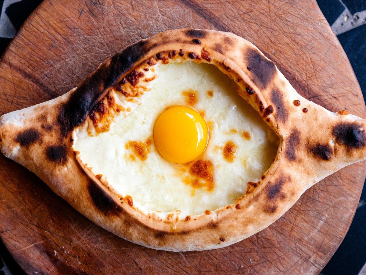 Khachapuri oder CHatschapuri mit Käse und Ei auf Holzbrett und Marmortisch. Draufsicht.