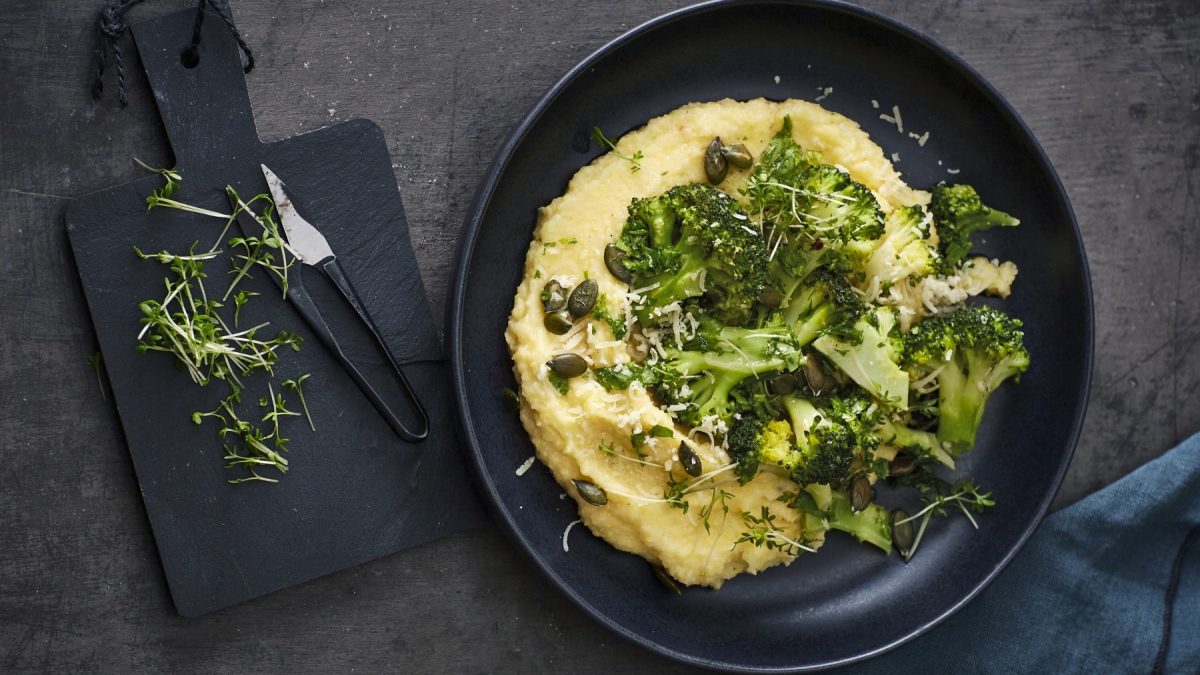 Polenta mit Kräuter-Brokkoli und Kürbiskernen, garniert mit frischem Parmesan und serviert auf einem dunklen Teller