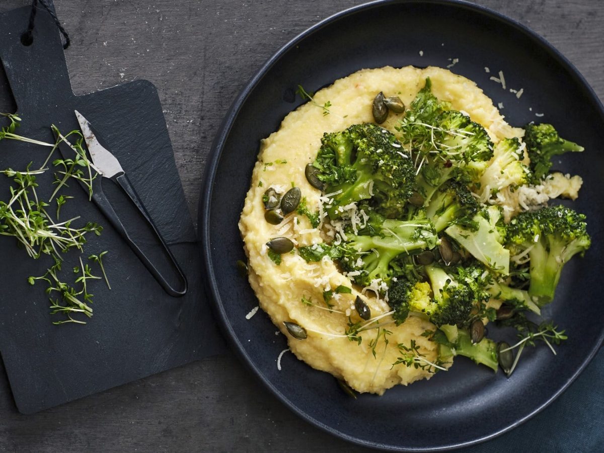 Polenta mit Kräuter-Brokkoli und Kürbiskernen, garniert mit frischem Parmesan und serviert auf einem dunklen Teller