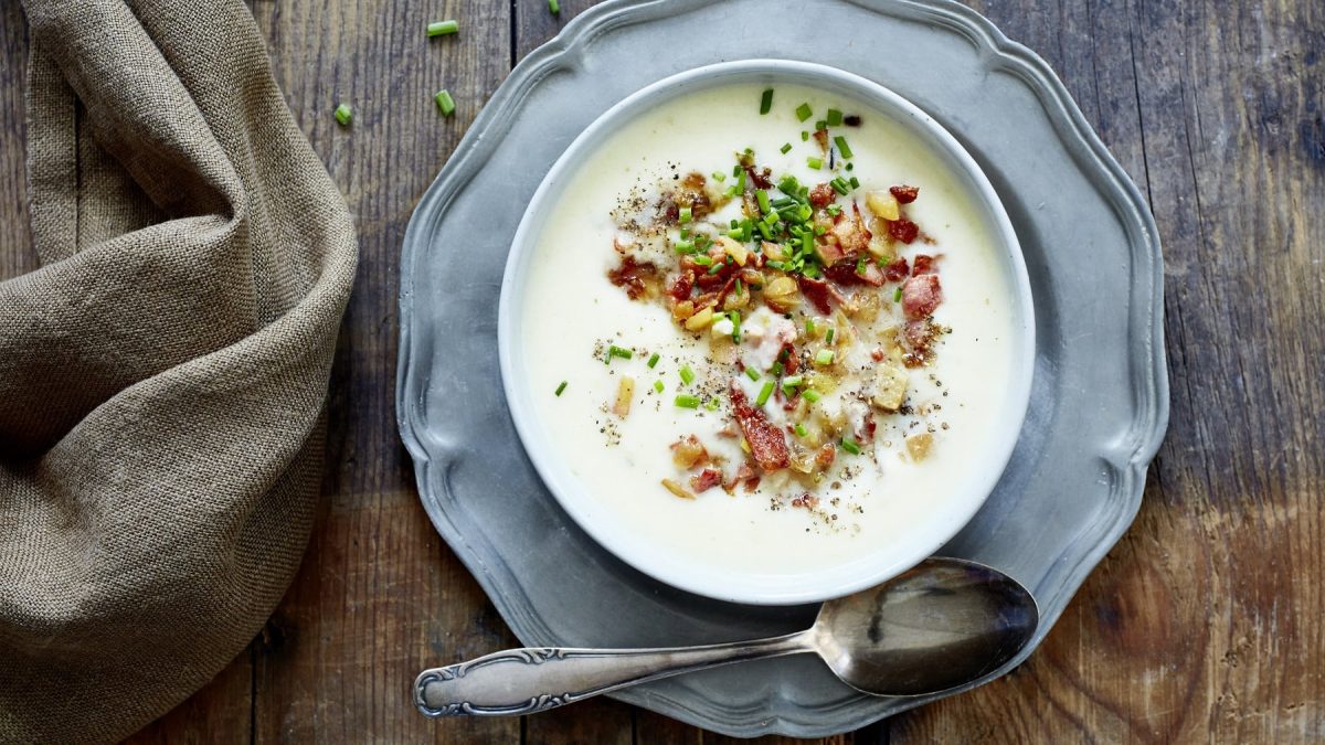 Selleriesuppe mit Apfel-Bacon-Salsa, garniert mit Schnittlauch und serviert in einer großen Suppenschale auf einem Holztisch.