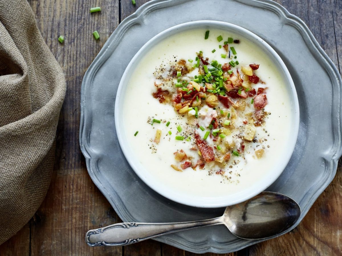 Selleriesuppe mit Apfel-Bacon-Salsa, garniert mit Schnittlauch und serviert in einer großen Suppenschale auf einem Holztisch.