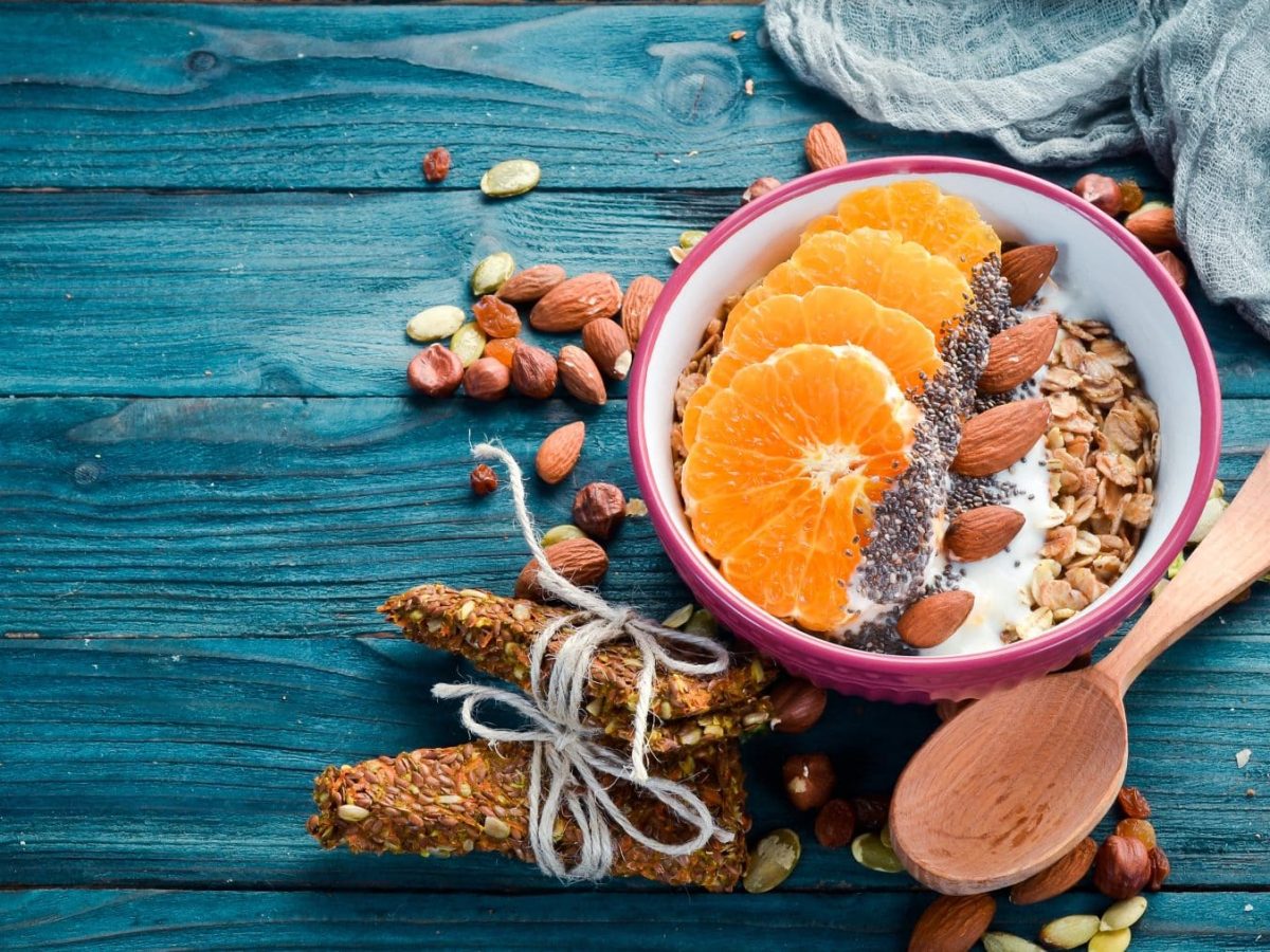 Vegane Superfood-Frühstücksbowl mit Mandarinen und Maracuja mit den Zutaten und Holzlöffel auf blauem Untergrund. Draufsicht.