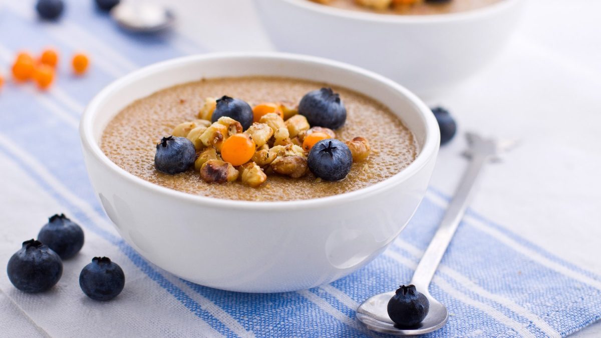 Eine weiße Schüssel mit dem Amaranth-Porridge auf einer weiß-blauen Tischdecke.