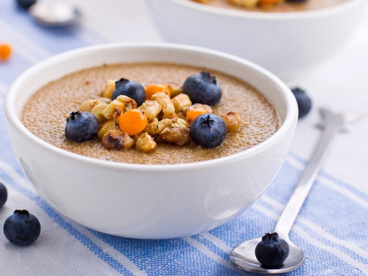 Eine weiße Schüssel mit dem Amaranth-Porridge auf einer weiß-blauen Tischdecke.