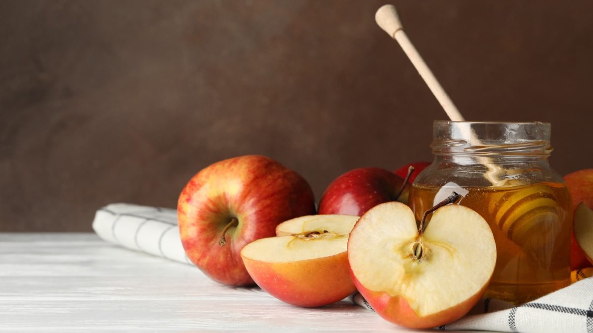 Ein paar Äpfel und ein Glas mit dem Apfel-Honig auf hellem Untergrund.