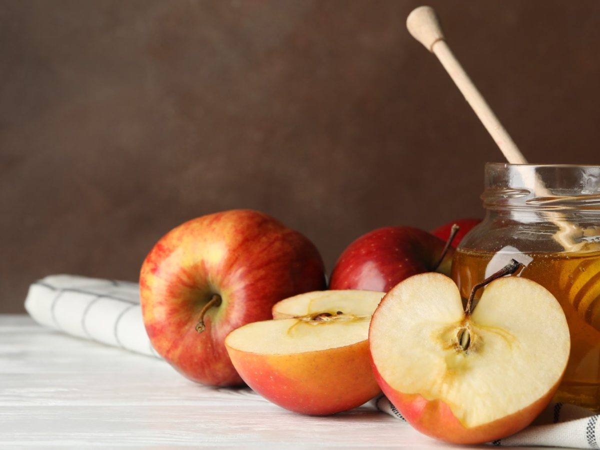 Ein paar Äpfel und ein Glas mit dem Apfel-Honig auf hellem Untergrund.