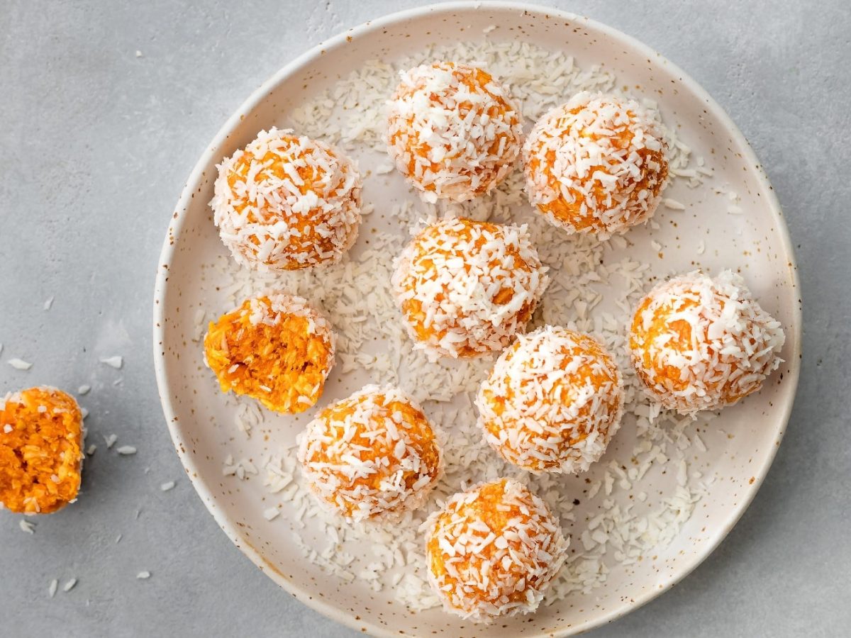 Mehrere der Aprikosen-Bällchen auf einem weißen Teller und grauem Untergrund.