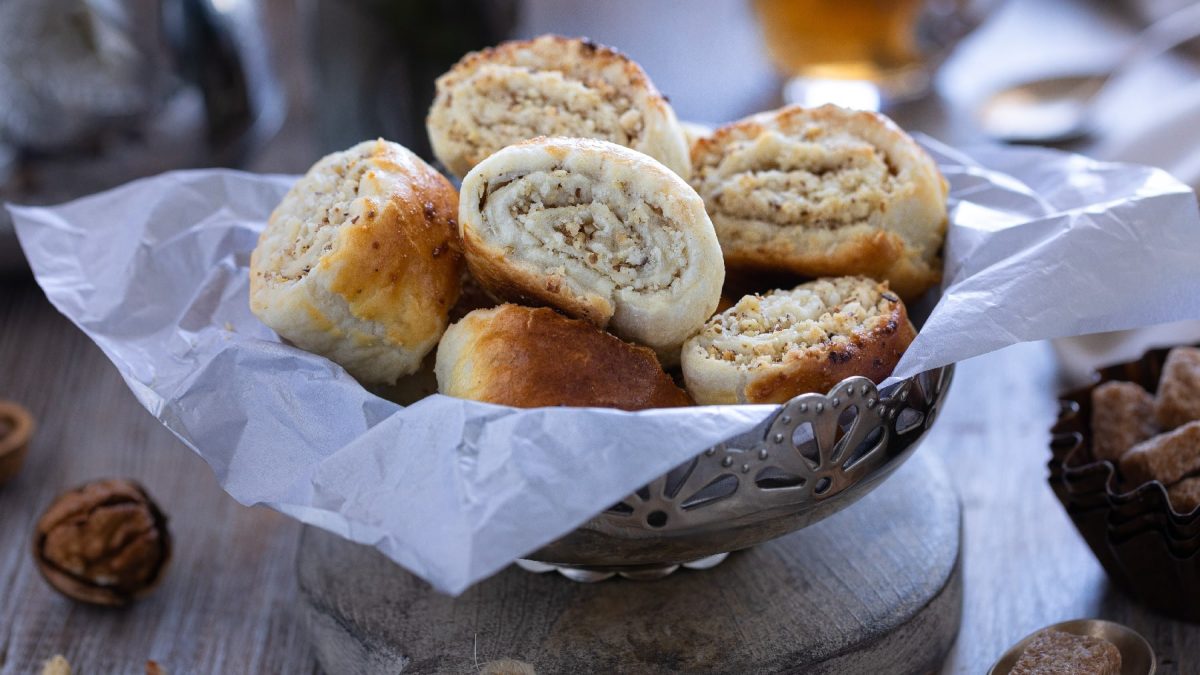 Eine silberne Schale mit den mit Nuss gefüllten Blätterteig-Schnecken auf einem rustikalen Holztisch.