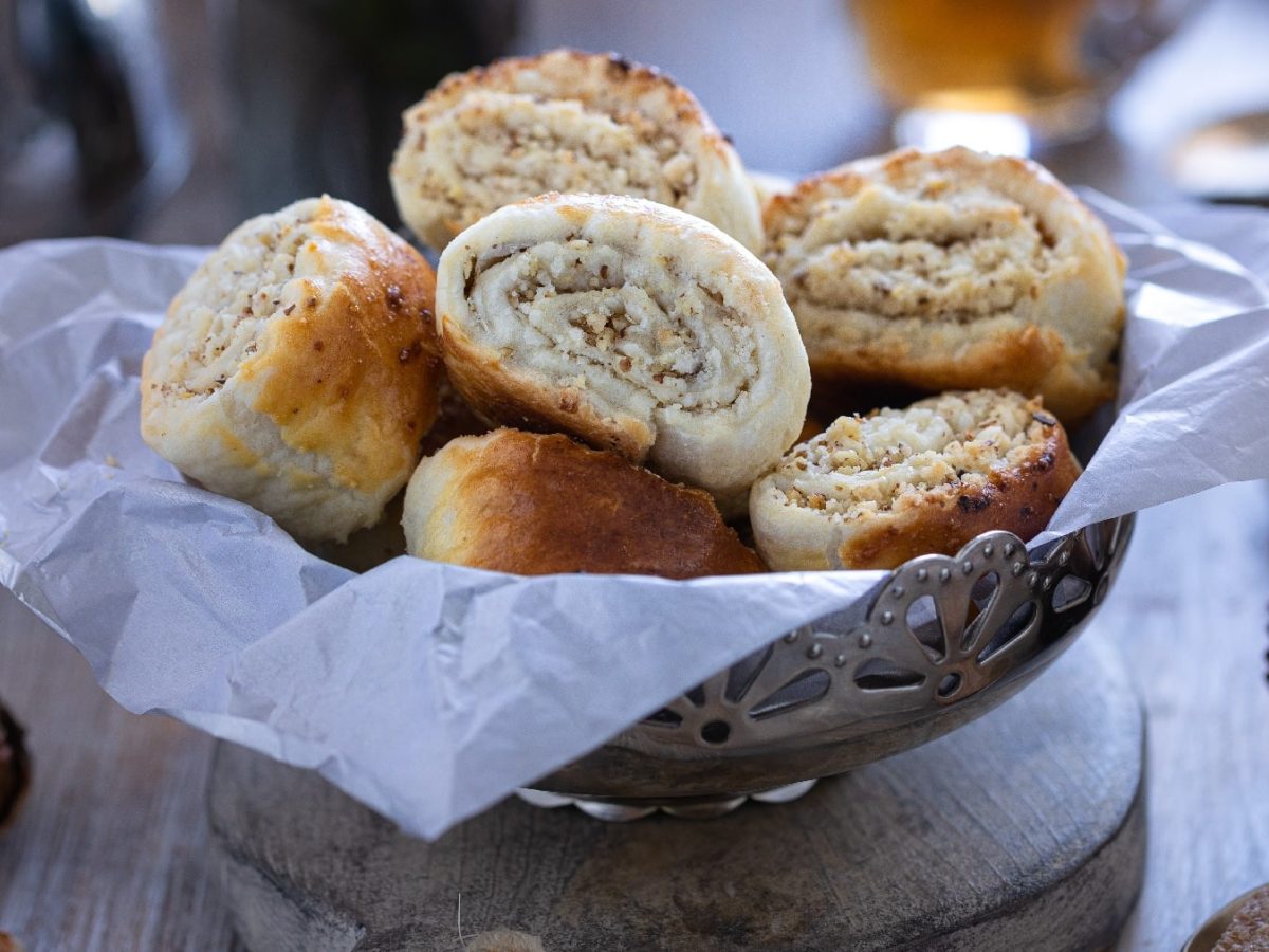 Eine silberne Schale mit den mit Nuss gefüllten Blätterteig-Schnecken auf einem rustikalen Holztisch.